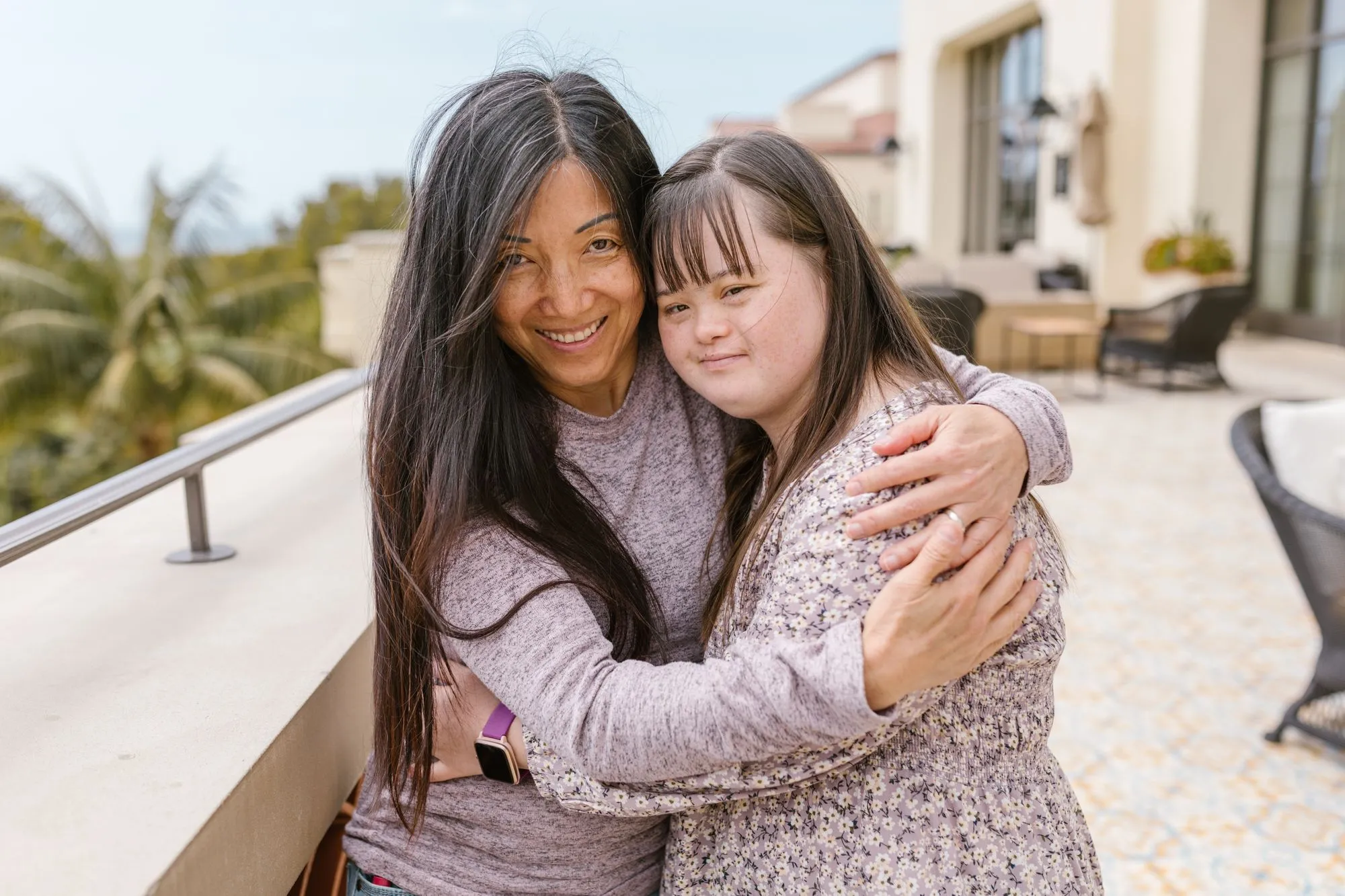 A mother and daughter hugging and smiling on a sunny patio